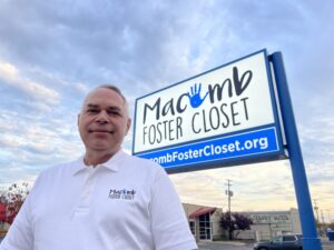 Kevin McAlpine in white shirt stands in front of Macomb Foster Closet sign.