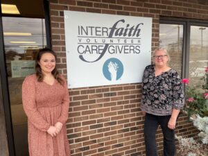 Exterior sign for Interfaith Volunteer Caregivers flanked by two staff members.